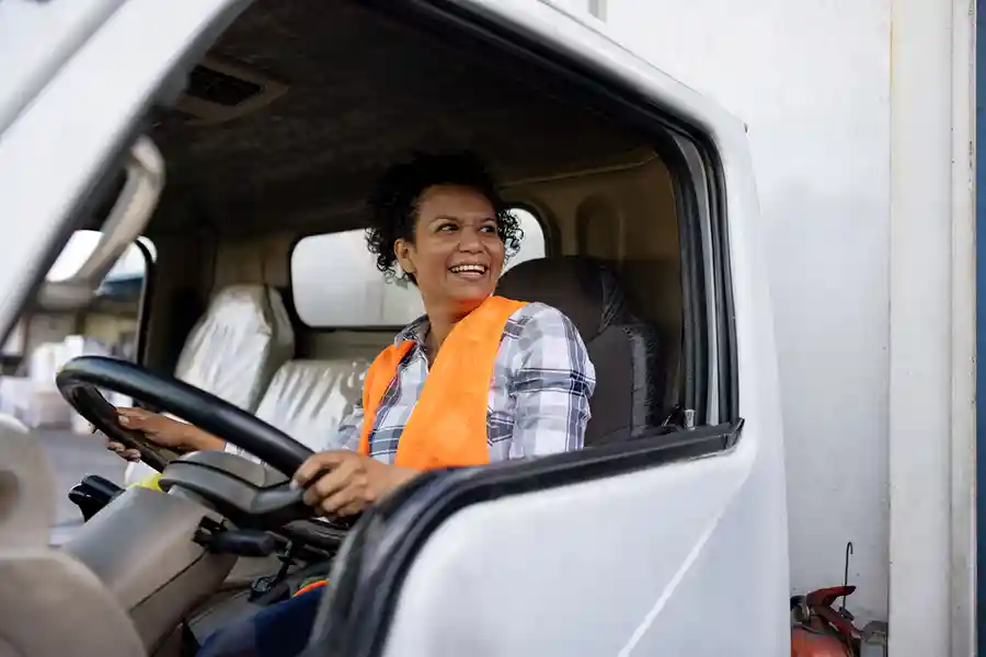 A woman in vest sitting in the cab of a semi truck 