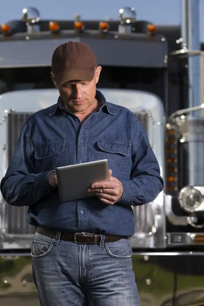 A truck driver in front of a semi working on an ipad