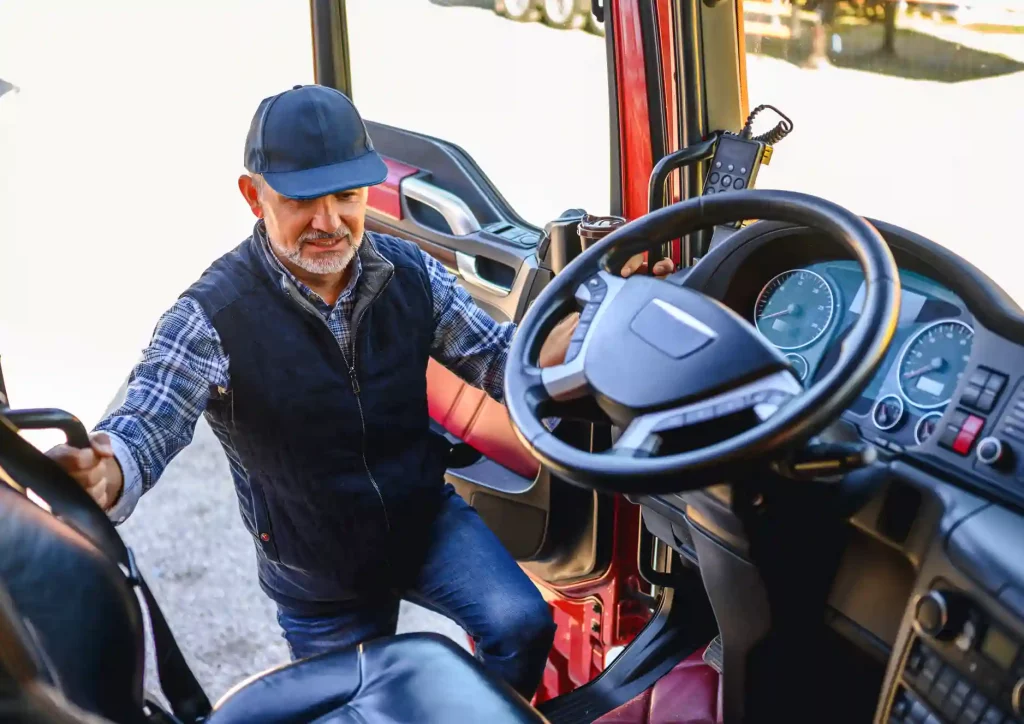 A middle aged trucker with cap and vest climbing into the cab of his semi